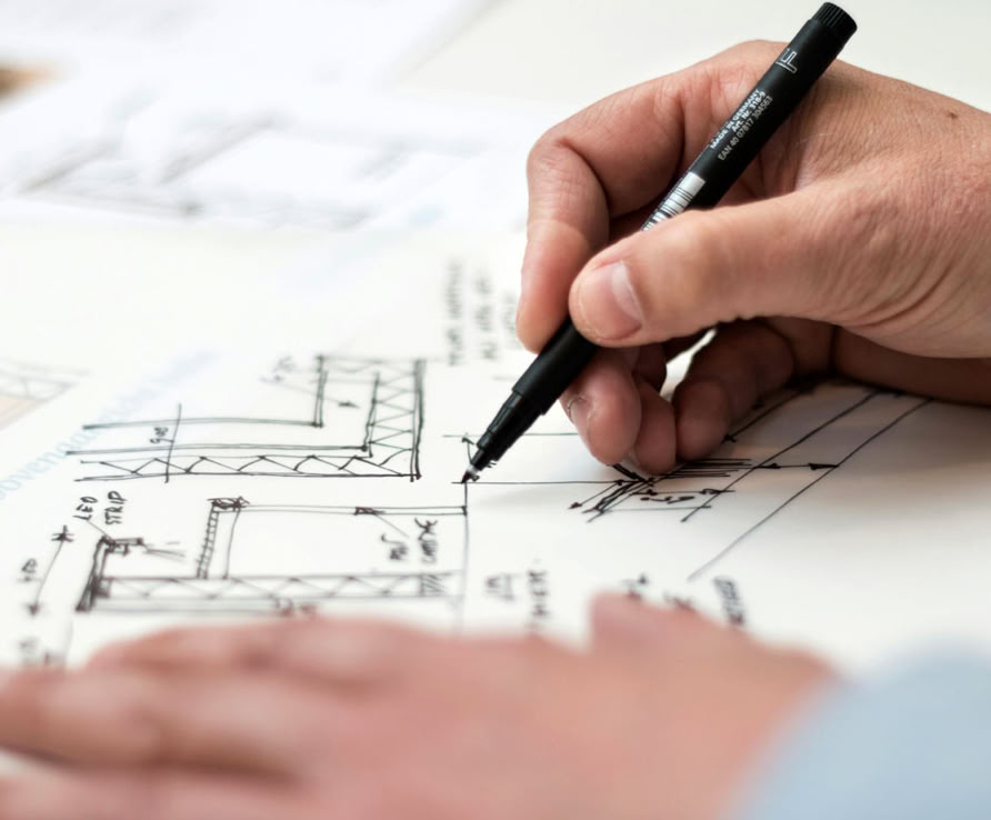 A person drawing architectural plans with a pen on a sheet of paper.